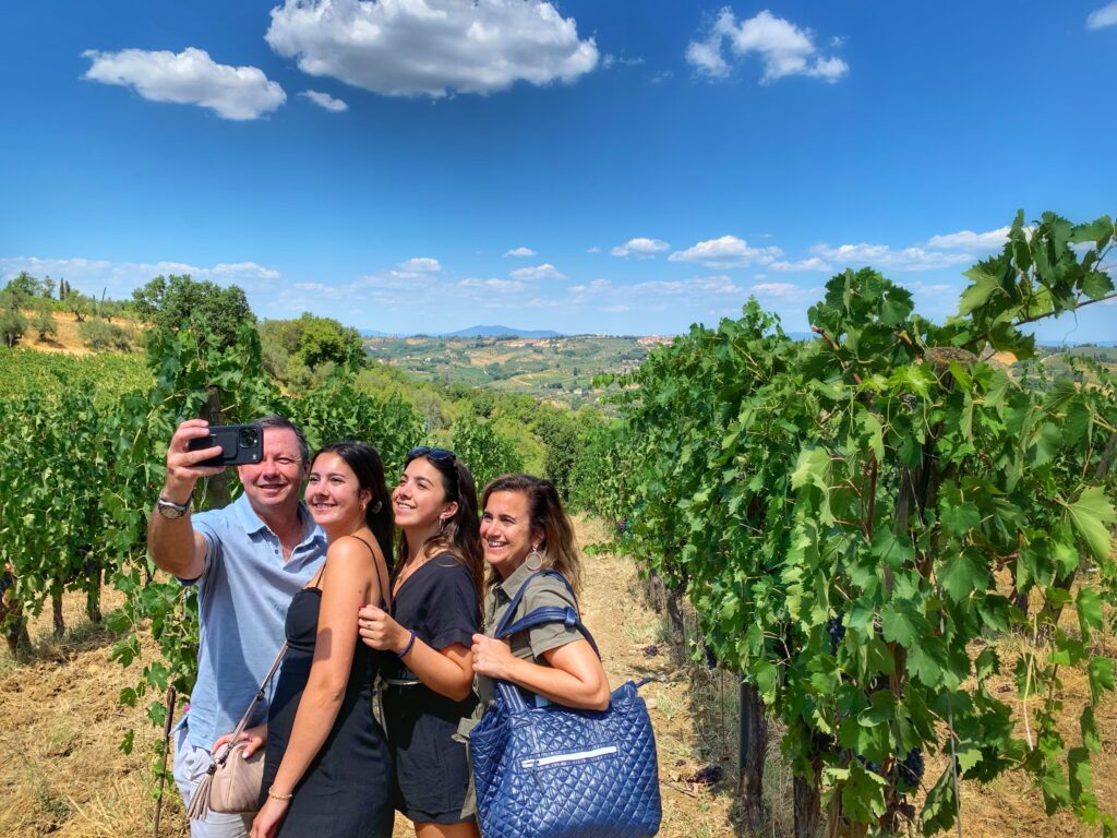 Family taking a selfie in a Tuscan vineyard in August, Tuscany: bright summer light and green canopies.