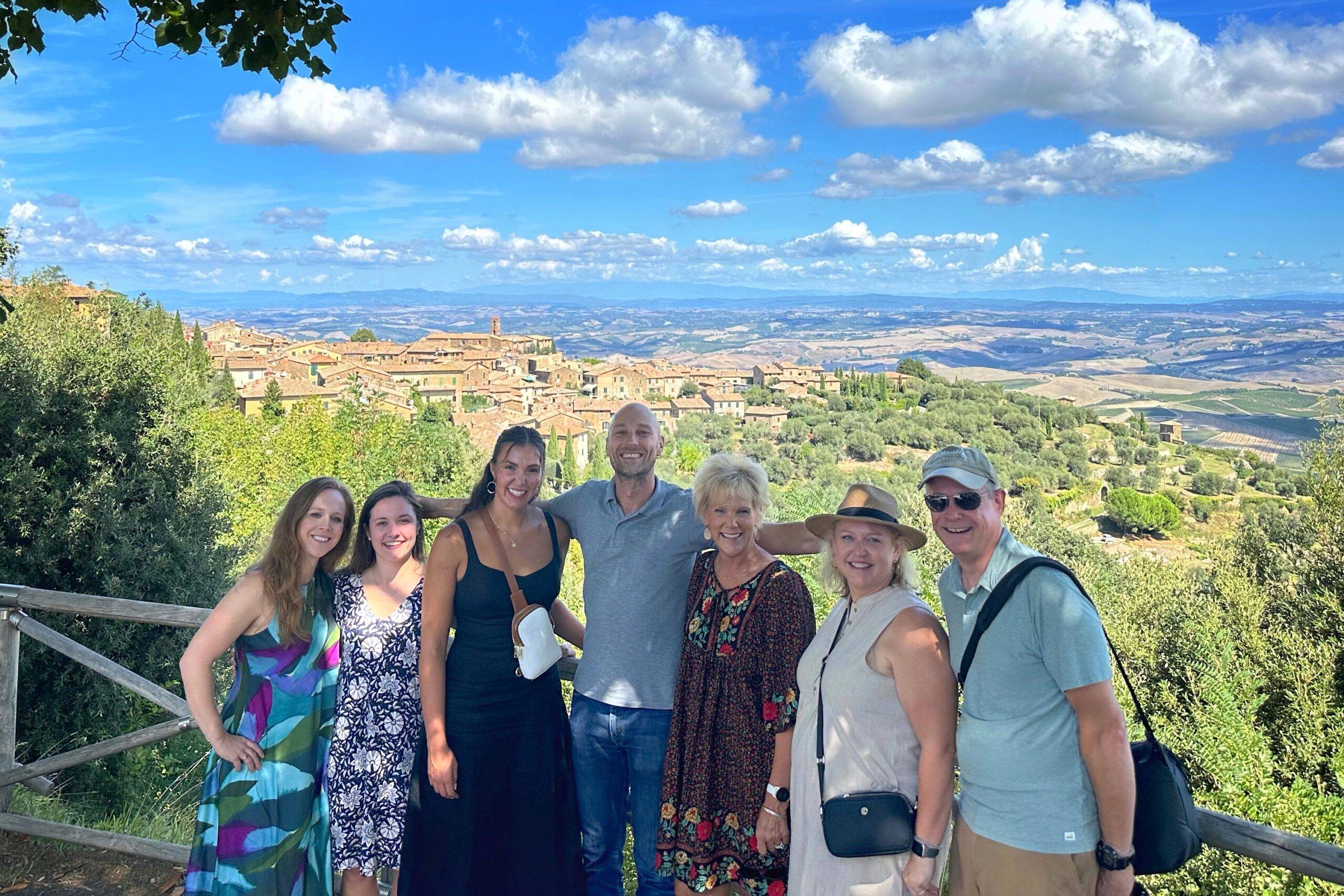 A small group on a Montalcino wine tour from Florence with the hilltop town of Montalcino in the background and their WSET wine educator guide in the center.
