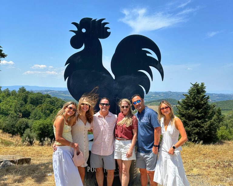 Guests posing beside the iconic Black Rooster symbol in Chianti Classico during a Tuscany wine tour, with rolling Tuscan hills in the background.